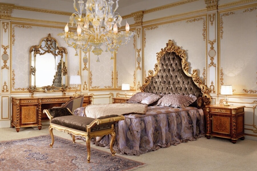 Luxury барокко в дизайне – интерьер спальни украшен золотыми деталями в виде лепнины на стенах, обрамления зеркала, изголовья кровати и центральной люстры